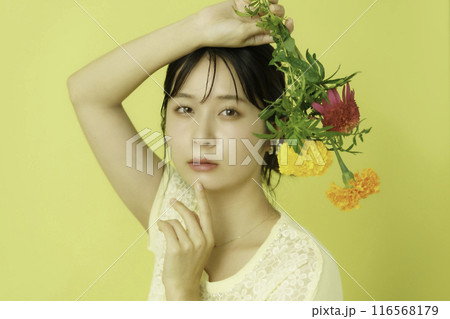 黄色背景の花を持つ若い女性のポートレート 116568179