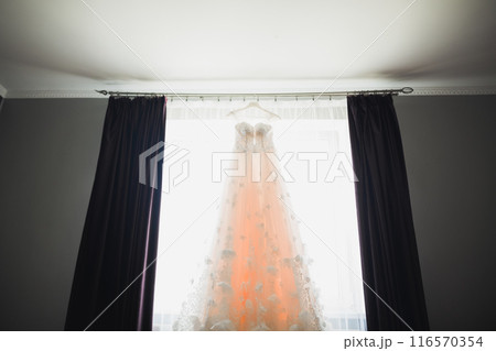 The perfect wedding dress with a full skirt on a hanger in the room of the bride The perfect wedding dress with a full skirt on a hanger in the room of the bride 116570354