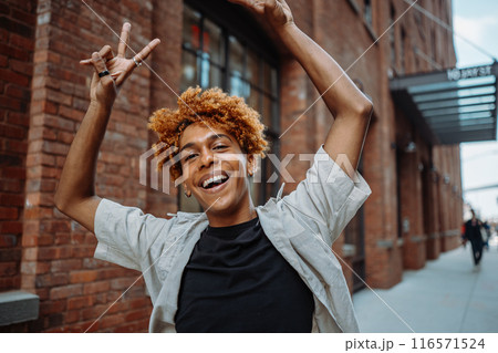 Cheerful person with curly hair posing in urban setting, radiating positivity and freedom 116571524