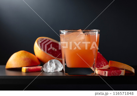 Glass of grapefruit juice with ice on a black background. 116571848