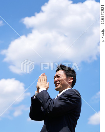 青空のもと手を合わせて祈る男性 116572921