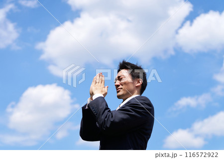 青空のもと手を合わせて祈る男性 116572922