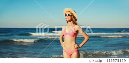 Summer vacation, beautiful happy slim woman in pink bikini swimsuit, tourist hat on the beach on sea 116573129