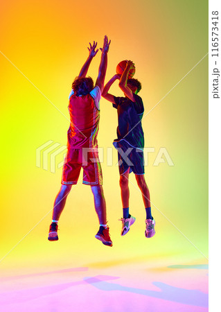 Two sportsmen, young man, train in basketball in neon light against gradient studio background, shows their hard work and agility 116573418