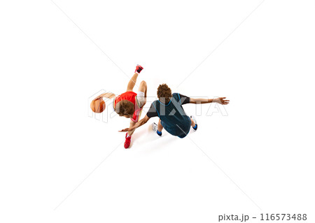 Player in red dribbling, while opponent in blue attempts to block him from ground against white studio background. Aerial view. 116573488