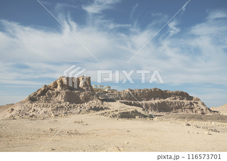 Ancient Desert Ruins Atop Rugged Hill Under Wispy Clouds 116573701
