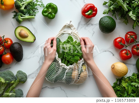 A man putting fresh vegetables and fruits in an eco-friendly mesh bag, avocados, tomatoes, sweet peppers, herbs 116573809