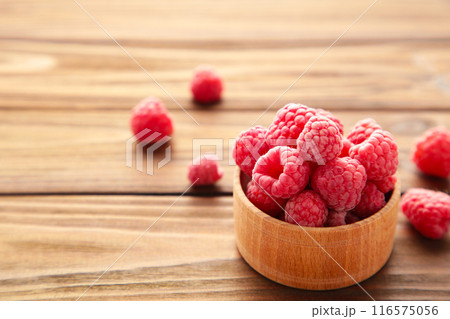 Ripe raspberries in wooden bowl on brown background. Top view 116575056