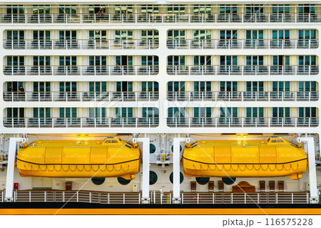 Side view of two yellow lifeboats and cabins balconies on a large cruise ship, ship safety equipment Side view of two yellow lifeboats and cabins balconies on a large cruise ship, ship safety equipment 116575228