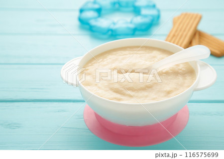 Bowl with baby food with toys on blue background Bowl with baby food with toys on blue background 116575699