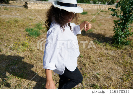 Woman in white shirt and straw hat walking outdoors on a sunny day 116578535