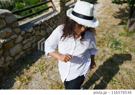 Person enjoying a walk outdoors wearing a white shirt and hat on a summer day 116578536