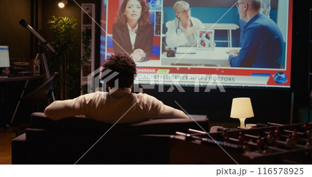 African american man watching news program on modern TV about artificial intelligence subject, zoom in close up shot. Cord cutter entertained by subscription service on ultrawide television screen African american man watching news program on modern TV about artificial intelligence subject, zoom in close up shot. Cord cutter entertained by subscription service on ultrawide television screen 116578925