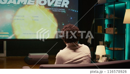 Upset african american gamer raging after losing game, playing on ultrawide smart TV. Man in living room feeling angry and shouting after his spaceship exploded, defeated in videogame Upset african american gamer raging after losing game, playing on ultrawide smart TV. Man in living room feeling angry and shouting after his spaceship exploded, defeated in videogame 116578926