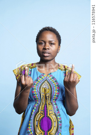 Vulgar aggressive woman giving the middle finger in studio, expressing irritation and frustration with offensive gesture sign over blue background. Girl being angry and obscene. Vulgar aggressive woman giving the middle finger in studio, expressing irritation and frustration with offensive gesture sign over blue background. Girl being angry and obscene. 116578941