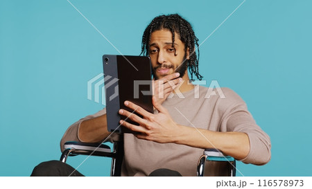 Person with paraplegia using tablet to post images on social media, doing selfie and writing photo caption. Man in wheelchair using online editing application on digital device, studio, camera B Person with paraplegia using tablet to post images on social media, doing selfie and writing photo caption. Man in wheelchair using online editing application on digital device, studio, camera B 116578973