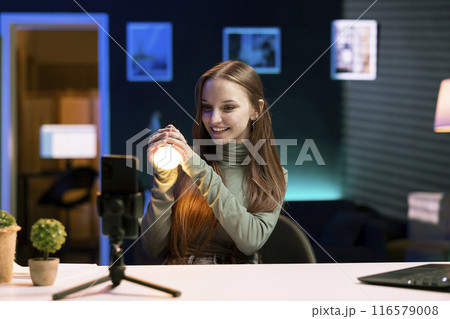 Cheerful young influencer filming review of light bulb able to change into different colors. Tech enthusiast showcasing smart home automation technology controlled by voice comwomands 116579008