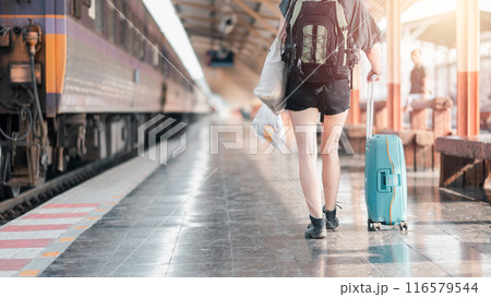A young traveler with a backpack and suitcase walking along a train platform, ready for an adventure at sunrise. A young traveler with a backpack and suitcase walking along a train platform, ready for an adventure at sunrise. 116579544