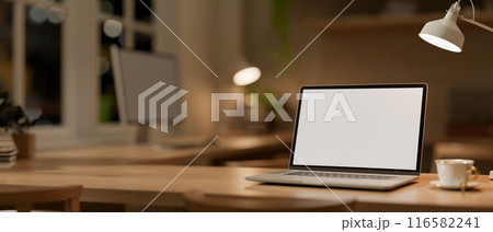 A wooden tabletop features a laptop mockup and accessories in a cozy contemporary office workspace. 116582241