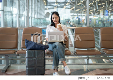 A beautiful Asian businesswoman sits at a waiting seat in the airport and working on her laptop. 116582326