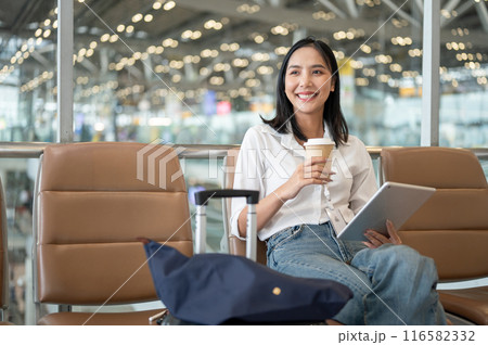Confident Asian woman sits at a waiting seat in the airport terminal, waiting for her boarding time. Confident Asian woman sits at a waiting seat in the airport terminal, waiting for her boarding time. 116582332