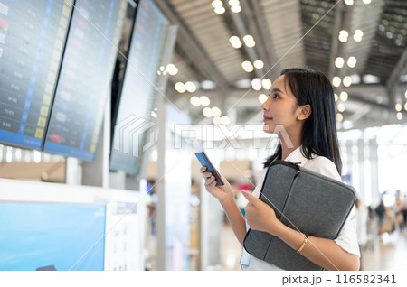 A beautiful Asian woman with her passport is standing in front of a flight information display. A beautiful Asian woman with her passport is standing in front of a flight information display. 116582341