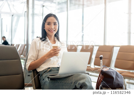 An attractive Asian female passenger sits in the airport terminal with her laptop and belongings. An attractive Asian female passenger sits in the airport terminal with her laptop and belongings. 116582346