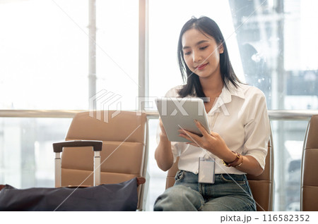 A charming Asian female passenger is working remotely, using her digital tablet in the airport. A charming Asian female passenger is working remotely, using her digital tablet in the airport. 116582352