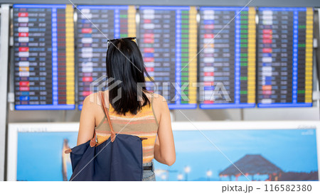 An Asian female tourist standing in front of a flight information display in the airport terminal. An Asian female tourist standing in front of a flight information display in the airport terminal. 116582380