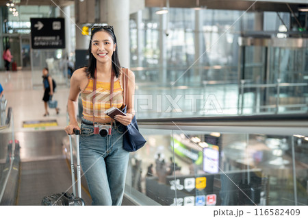 A beautiful Asian female tourist with her luggage is on the airport escalator, traveling by plane. 116582409