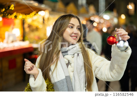 Woman at New Year fair and bustle is leisurely examining ball for decorating Christmas tree. Woman at New Year fair and bustle is leisurely examining ball for decorating Christmas tree. 116582546