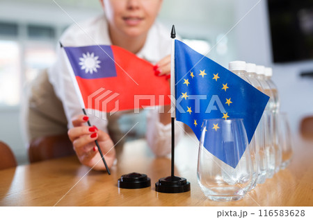 Woman secretary prepares an office for negotiations - she places flags of European Union and Taiwan table 116583628