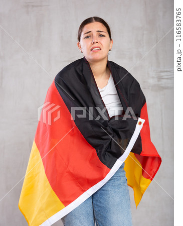 Sad young female student with flag of Germany against of gray wall background Sad young female student with flag of Germany against of gray wall background 116583765