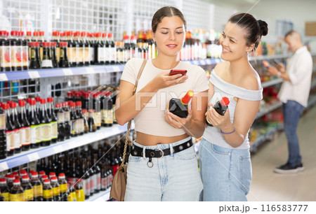 Two female friends choose soy sauce in Chinese supermarket. Read the QR code from the label using smartphone 116583777