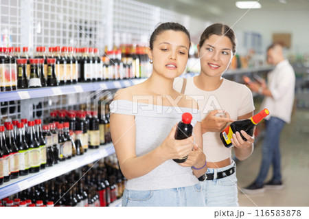 Two female friends choose soy sauce in Chinese supermarket. Read the QR code from the label using smartphone 116583878