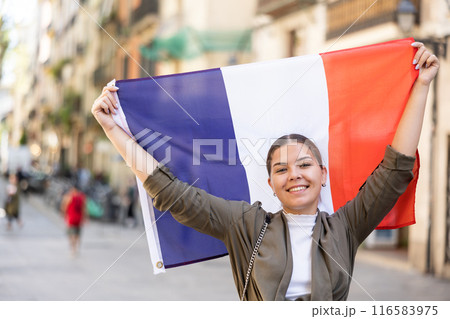 Happy young woman waving the flag of France on city street 116583975