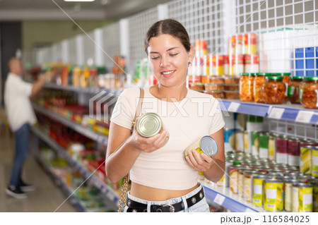 Young woman choosing canned food in store 116584025