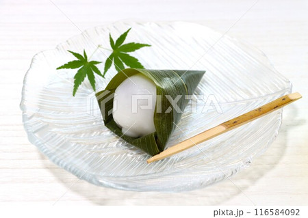 ガラス皿に青紅葉と笹の葉に包まれた水まんじゅうをのせて 116584092