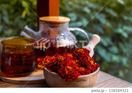 Marigold flower healthy tea in glass mug with tea pot on garden table. Herbal medicine Delicious tisane tea with fresh yellow blossom dandelion flowers tea cup. Green clearing infusion Wildflowers 116584321