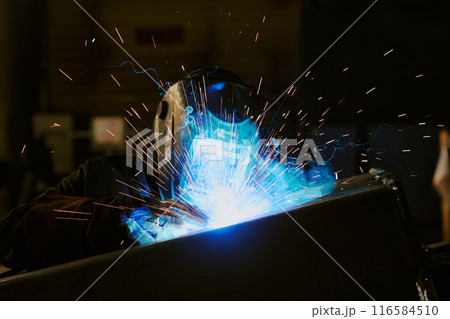 Unrecognizable professional welder wearing helmet doing metalwork with use of torch, medium closeup shot 116584510