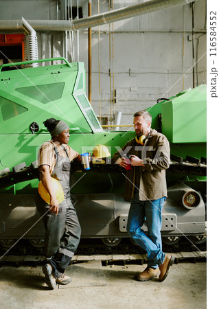 Vertical shot of young ethnically diverse male and female engineers chatting during lunch break at work in factory, copy space 116584552