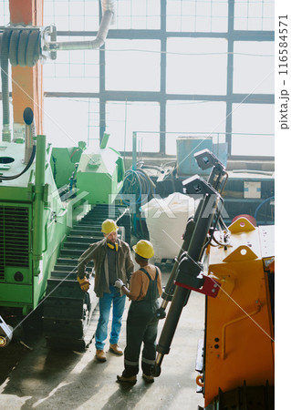 High angle view shot of two ethnically diverse male and female engineers having conversation at work in dozer production factory High angle view shot of two ethnically diverse male and female engineers having conversation at work in dozer production factory 116584571