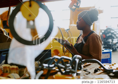 Young African American factory worker checking industrial machine and using digital tablet 116584713