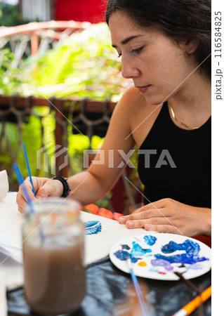 Woman concentrating while painting with a brush in a summer workshop. Vertical Woman concentrating while painting with a brush in a summer workshop. Vertical 116584825