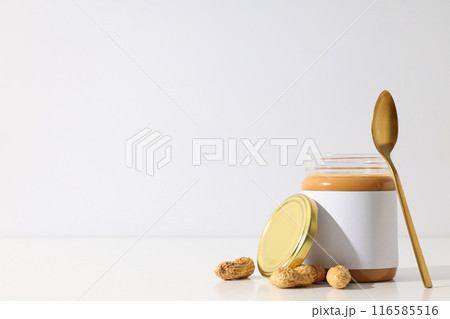 Peanut paste in a glass jar with a spoon, on a light background. Peanut paste in a glass jar with a spoon, on a light background. 116585516
