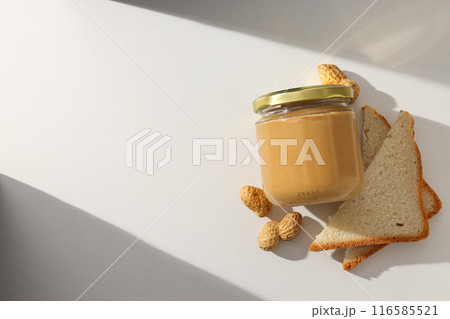 Peanut paste in a glass jar with toast, on a light background. 116585521