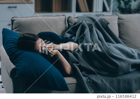 A woman with a cold with pills is treated at home chooses which drugs to take and self-medicates, checks the expiration date while sitting on the couch at home 116586412