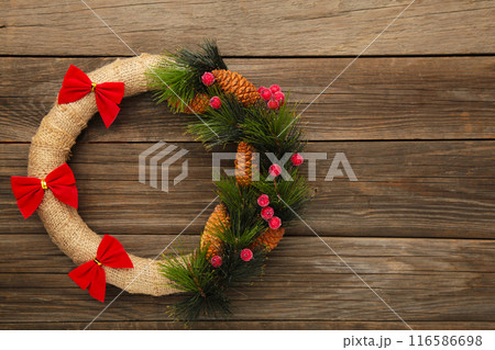 Green christmas wreath decorated with red bow on grey wooden background. Thanksgiving Day. Green christmas wreath decorated with red bow on grey wooden background. Thanksgiving Day. 116586698