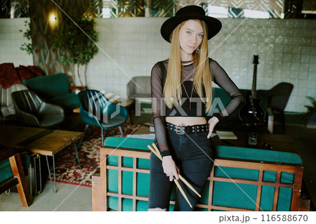 Young Caucasian rock musician holding drumsticks standing relaxed in room in abandoned house looking at camera 116588670