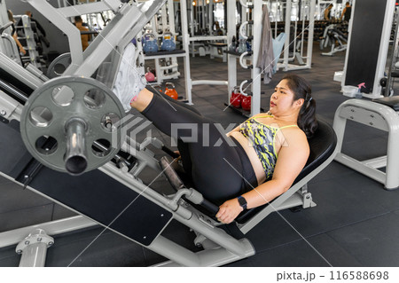 Young overweight woman using leg press machine to work on her legs strength at a local gym 116588698